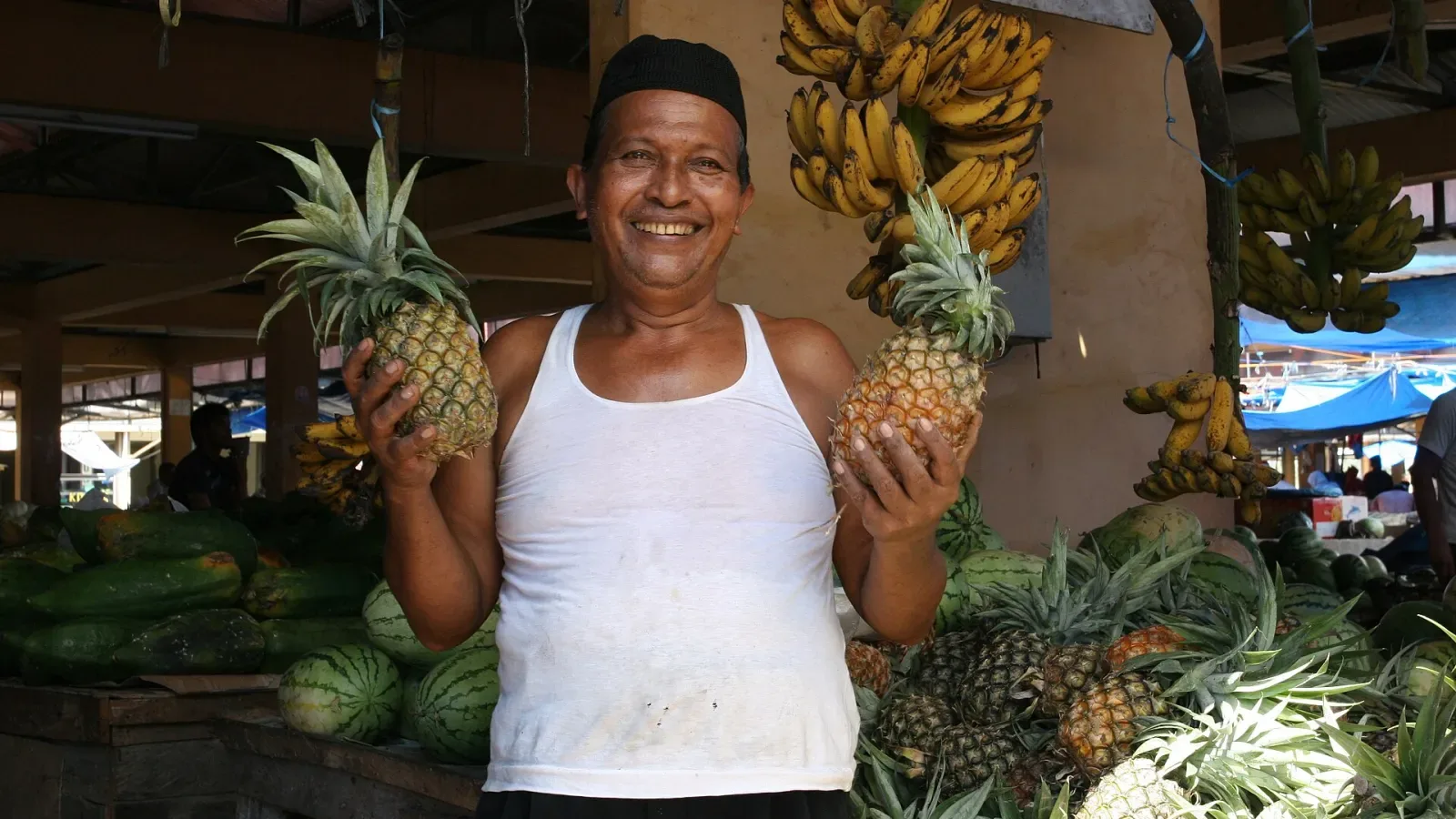 Pedagang buah tersenyum memegang dua nanas di kios pasar tradisional